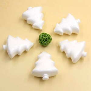 May include: Five white foam Christmas tree shapes, each with a different orientation, are arranged in a circle on a beige surface. A small green ball is in the centre of the circle.