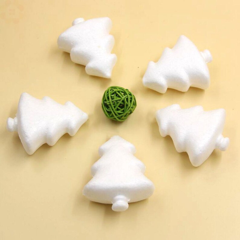May include: Five white foam Christmas tree shapes, each with a different orientation, are arranged in a circle on a beige surface. A small green ball is in the centre of the circle.