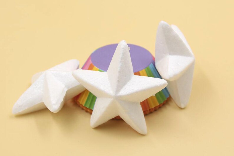 May include: Three white foam star shapes on top of a rainbow cupcake liner. The stars are 3-dimensional and have a slightly textured surface.
