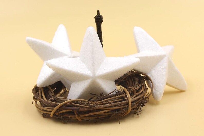 May include: Three white foam star ornaments arranged in a wreath of brown twigs. The stars are arranged with points facing outward, creating a circular shape.