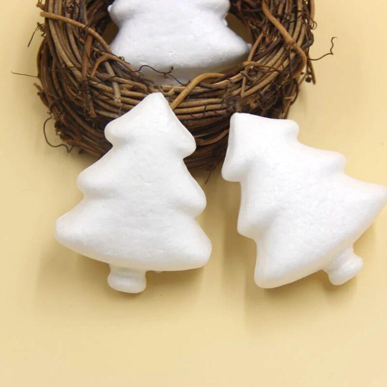 May include: Three white foam Christmas tree shapes. The trees are sitting on a light brown surface.