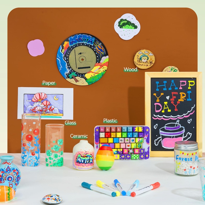 Pode incluir: Um conjunto de marcadores coloridos com uma variedade de superf&iacute;cies para colorir, incluindo vidro, cer&acirc;mica, papel, madeira e pl&aacute;stico. As superf&iacute;cies s&atilde;o decoradas com desenhos e as palavras "Happy Friday".