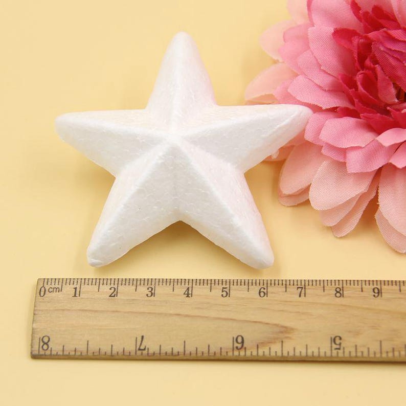 May include: A white foam star measuring approximately 6 inches across. The star is sitting on a wooden ruler with centimeter markings.