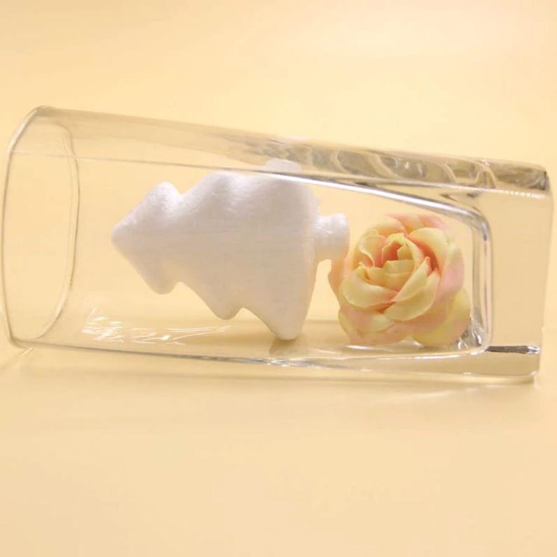 May include: A clear glass vase containing a white styrofoam Christmas tree and a yellow and pink rose.