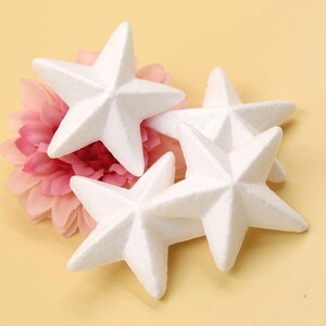 May include: Four white foam star shapes, each with five points, are arranged in a cluster. The stars are a light white color and have a slightly textured surface.