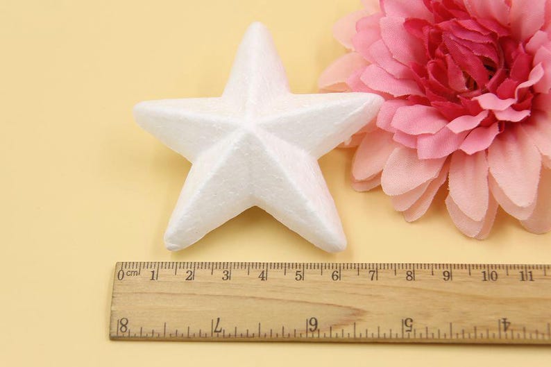 May include: A white foam star measuring 6 inches across. The star is sitting on a yellow surface next to a pink flower and a wooden ruler.
