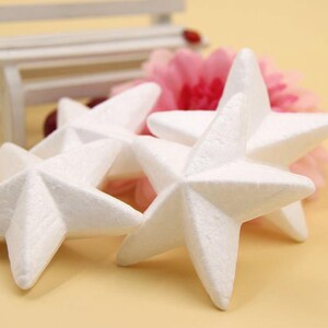 May include: Four white foam star shapes arranged on a light brown surface. The stars are slightly overlapping and have a textured surface.