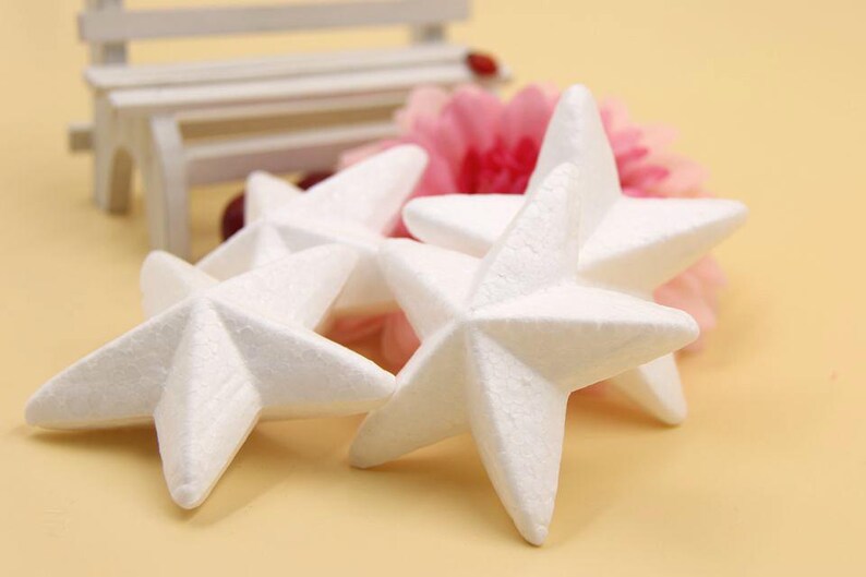 May include: Four white foam star shapes arranged on a light brown surface. The stars are slightly overlapping and have a textured surface.