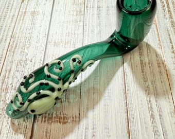 May include: A translucent emerald green glass pipe featuring a curved stem and a deep bowl. The exterior of the stem is decorated with a pale green, raised octopus-like design with small black dots accenting the swirling tentacles.