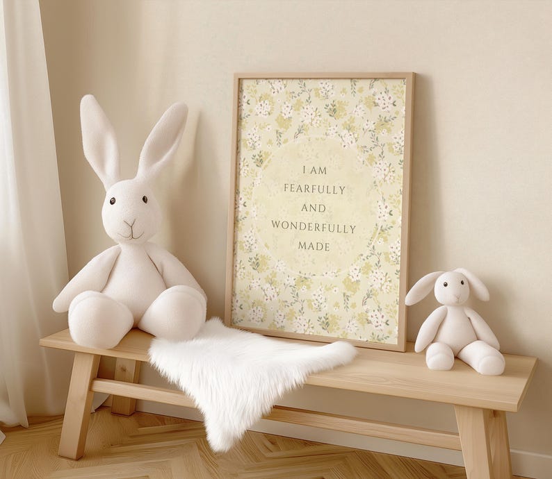 May include: A white wooden bench with a white faux fur throw on top. A white stuffed bunny sits on the bench. A framed print with a floral design and the text "I am fearfully and wonderfully made" hangs on the wall behind the bench.