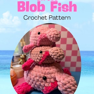 May include: A stack of three pink crocheted blob fish toys with black eyes and bright pink accents. The toys are on a blue surface with the text "Stress Blob Fish Crochet Pattern" in pink.