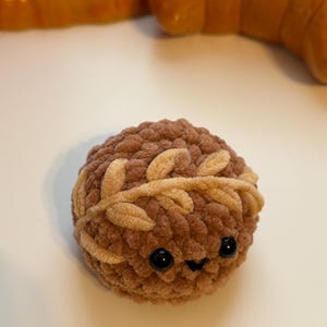 May include: A brown crocheted plush toy with a smiling face and a brown and beige crocheted wreath around its head.