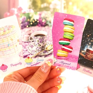 May include: Four rectangular oracle cards featuring dessert and beverage imagery. The first card shows a cake with the text Prosperity. The second displays a teacup with the text Gossip. The third shows stacked macarons with the text Alignment. The fourth depicts a teacup in a starry scene with the text Restless.