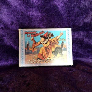 Puede incluir: Una baraja de cartas místicas vintage "Madame Le Normand". La caja presenta una ilustración de una figura disfrazada con un búho, un gato negro y el texto "Cards for". El fondo es de terciopelo morado.