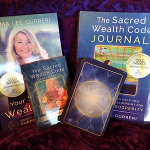 Könnte beinhalten: Eine Auswahl an spirituellen Büchern und Orakelkarten. Zu den Büchern gehören "The Sacred Wealth Code Journal" und "Your Sacred Wealth Code". Die Orakelkarten sind in einem Deck mit blauem und goldenem Design. Alle Artikel liegen auf einer dunkelvioletten Oberfläche.