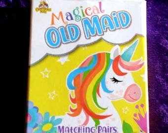 May include: A boxed card game titled "Magical Old Maid" featuring a unicorn illustration with a rainbow mane. The box is yellow with blue and pink accents, and the game is for ages 4+ and 2 or more players.