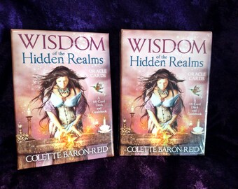 May include: Two oracle card decks titled "Wisdom of the Hidden Realms" by Colette Baron-Reid. The covers feature a woman in a corset, with long dark hair, and a hummingbird. The text includes "Oracle Cards" and "44-Card Deck and Guidebook."