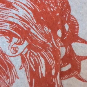 Pu&ograve; includere: Primo piano di un disegno stampato in rosso e bianco su un tessuto bianco. Il disegno presenta un'immagine stilizzata di un viso con capelli lunghi.