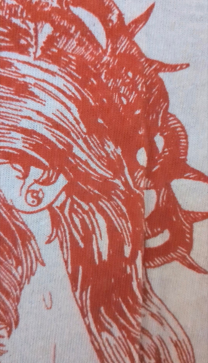 Pu&ograve; includere: Primo piano di un disegno stampato in rosso e bianco su un tessuto bianco. Il disegno presenta un'immagine stilizzata di un viso con capelli lunghi.