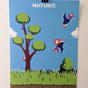 May include: A pixelated art print with the word "NATURE" at the top. The artwork depicts a blue sky, green grass, a brown tree, and two birds in flight. The style is reminiscent of retro video games.