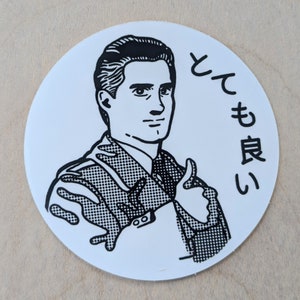May include: A white, circular sticker featuring a black and white illustration of a man giving a thumbs-up. The man is wearing a suit jacket. Japanese text is printed in black above the man's head.