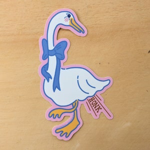 May include: A white goose with a blue bow around its neck is walking with its wings out. The goose has a pink outline and is on a light brown background. The goose is honking and the word "HONK" is written in brown letters.