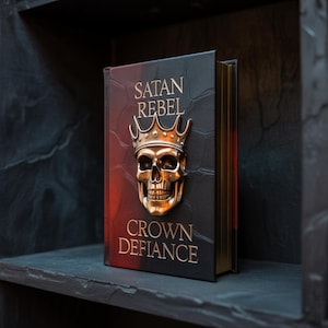 Può includere: Un libro intitolato "SATAN REBEL CROWN DEFIANCE" con un emblema di teschio e corona dorata. Il libro ha una copertina in pelle nera con scritte dorate e un gradiente rosso sui bordi. Il libro è esposto su una mensola scura.