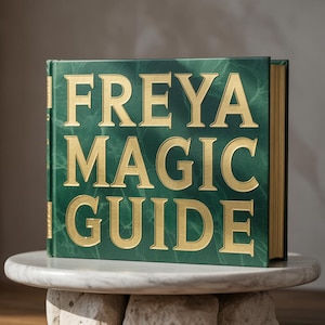 May include: A hardcover book with the title "FREYA MAGIC GUIDE" in gold lettering on a green cover. The book is displayed on a round, marble-like surface.