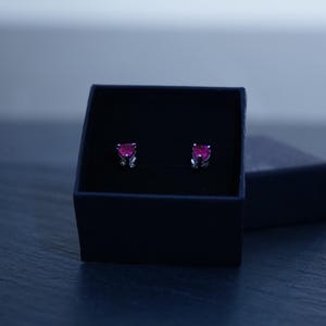 Könnte beinhalten: Ein Paar herzförmige Rubinohrringe in einer schwarzen Samt-Schmuckschatulle.