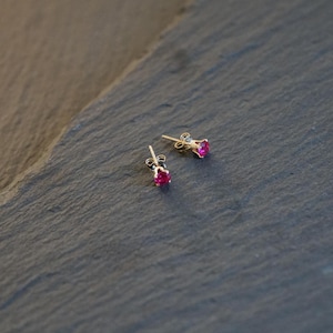 Könnte beinhalten: Ein Paar goldene Ohrstecker mit kleinen, leuchtend pinkfarbenen Edelsteinen.