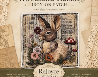 May include: A square iron-on patch featuring a brown rabbit sitting among colorful flowers and mushrooms. The background of the patch has a vintage newspaper print. The text on the patch packaging reads Woodland Rabbit, Iron-On Patch, and ReJoyce Studio AZ.