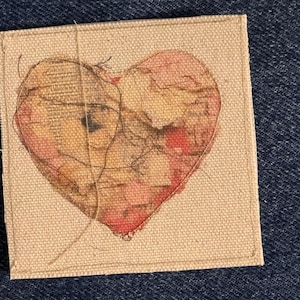 May include: A heart-shaped piece of art on a canvas background. The heart is made of paper with a layered, textured look and is painted in shades of pink, brown, and white.