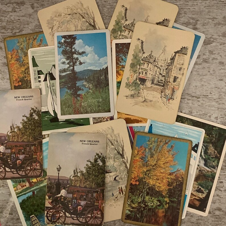 May include: A collection of rectangular vintage postcards featuring various scenes including New Orleans French Quarter street views with horse-drawn carriages, colourful autumn landscapes, sailboats on water, and ink-style architectural sketches.