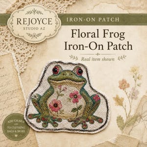 May include: An iron-on patch featuring a green frog with red eyes and pink floral patterns on its body. The patch has a black stitched border and is displayed on a background with the text REJOYCE STUDIO AZ, Floral Frog Iron-On Patch, and Real item shown.