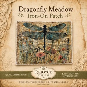 May include: A rectangular iron-on patch featuring a detailed illustration of a blue dragonfly hovering over a field of pink and orange wildflowers. The text Dragonfly Meadow Iron-On Patch is printed above the patch, with Rejoyce Studio AZ below.