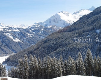 May include: A snowy mountain range with a forest of evergreen trees in the foreground. The text "Teach Áine" is visible in the lower right corner of the image.