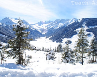 May include: A snowy mountain landscape with a valley covered in snow and several evergreen trees in the foreground. The sky is blue and clear.