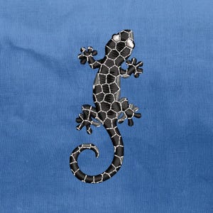 May include: An embroidered lizard design in black and white, featuring a geometric pattern on its body, is displayed against a solid blue background. The lizard's tail curls, and its feet are detailed. The embroidery adds texture and dimension to the design.