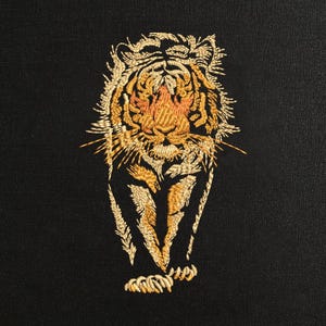 May include: Embroidered tiger design in shades of gold, orange, and tan on a black background. The tiger is depicted in a frontal pose, showcasing intricate details in its fur and facial features. The embroidery creates a textured, three-dimensional effect.