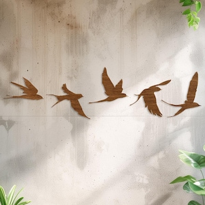 Puede incluir: Un conjunto de seis siluetas de pájaros de madera en vuelo, dispuestas en fila en una pared gris claro. Los pájaros están todos mirando en la misma dirección y están hechos de madera marrón claro. La pared es texturizada y tiene un ligero brillo. Hay dos plantas en macetas en primer plano, una a la izquierda y otra a la derecha. El suelo está hecho de tablones de madera marrón claro.