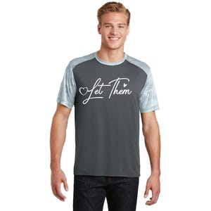 May include: Dark grey athletic t-shirt featuring the white script text "Let Them". The shirt has light grey mesh sleeves and a crew neck. The material is designed to wick away moisture.