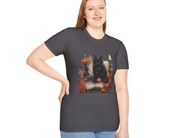 May include: Dark gray t-shirt featuring a detailed illustration of a black cat sitting on books surrounded by pumpkins and autumn leaves. A candle and decorative elements complete the fall-themed design.