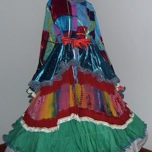 May include: A colorful, multi-layered skirt with a blue, red, and green color scheme. The skirt has a ruffled hem and a lace trim. The skirt is worn over a blue, red, and green patterned top with a lace collar.
