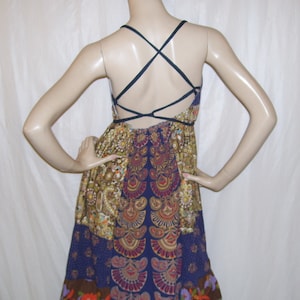 May include: A blue and gold patterned dress with a criss-cross back strap. The dress has a short, flowy skirt with a brown trim.