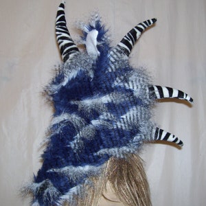 May include: A blue and white faux fur headpiece with black and white striped horns. The horns are made of fabric and are attached to the headpiece with a wire frame.