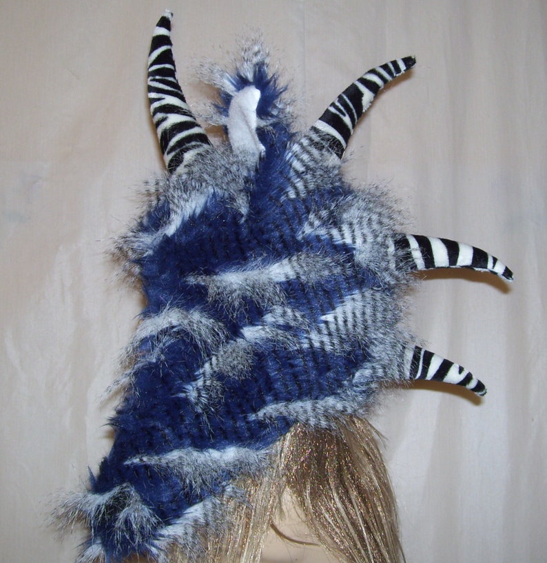 May include: A blue and white faux fur headpiece with black and white striped horns. The horns are made of fabric and are attached to the headpiece with a wire frame.