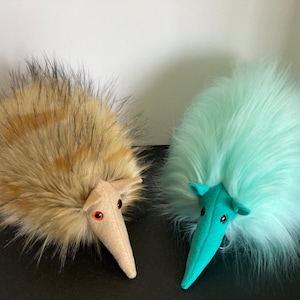 May include: Two plush animal toys. One is brown and tan with black accents, the other is light blue. Both have long, fluffy fur, long snouts, and small, round eyes. The toys are on a black surface.