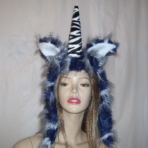May include: A blue and white faux fur hooded hat with a zebra print unicorn horn. The hat is worn on a mannequin head with long blonde hair.