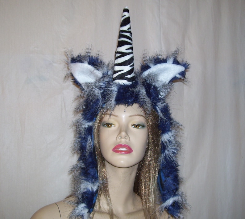 May include: A blue and white faux fur hooded hat with a zebra print unicorn horn. The hat is worn on a mannequin head with long blonde hair.