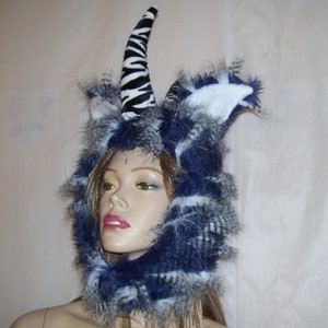 May include: A blue and white furry hooded hat with a zebra-print horn. The hat is worn by a mannequin with a neutral expression.